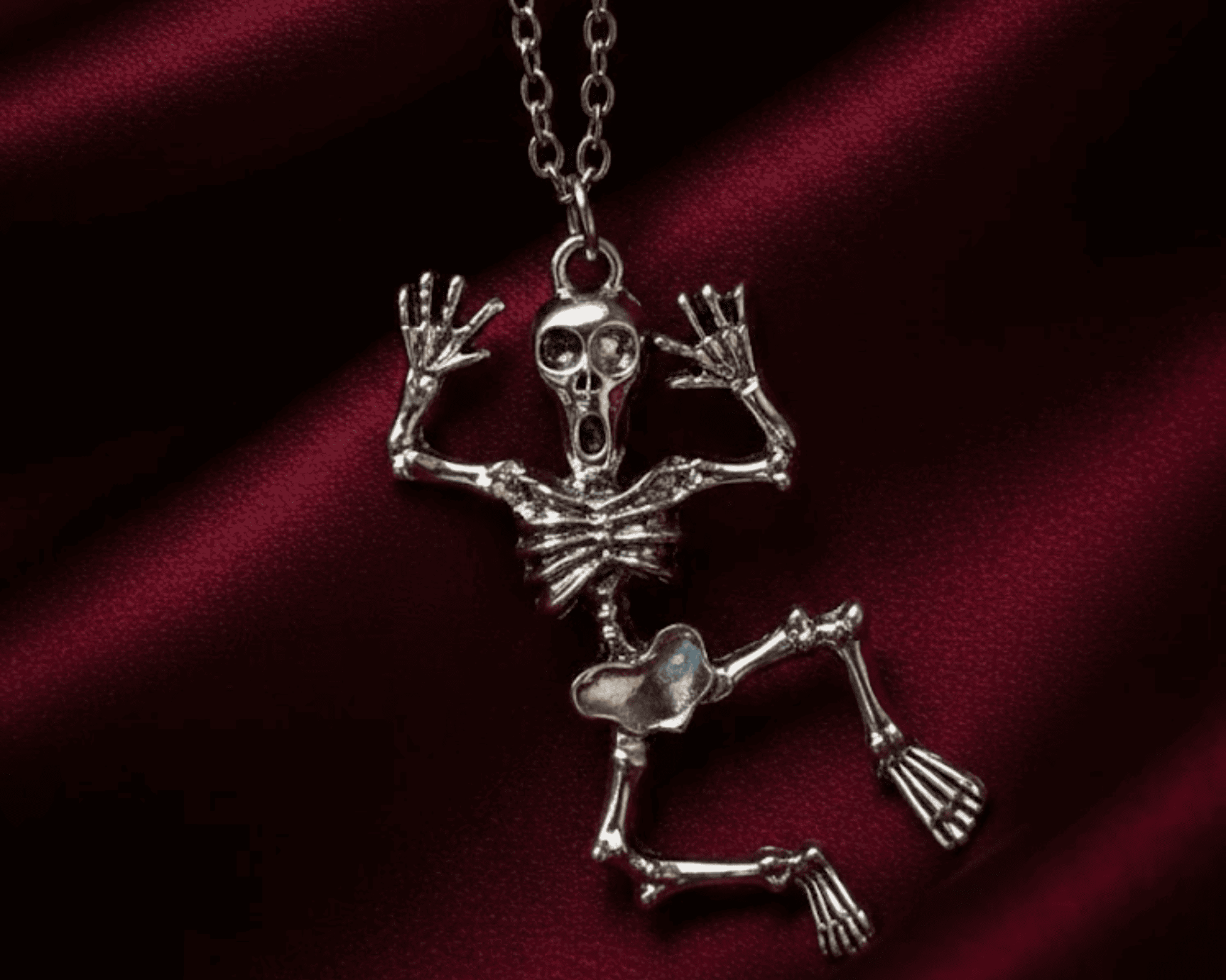 Silver skeleton pendant necklace on a red satin background